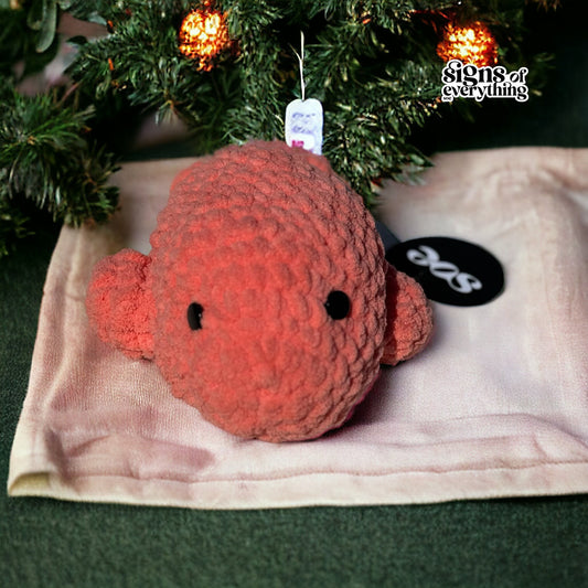 Red knitted monkey ornament with a tag on a beige blanket against a Christmas tree background.